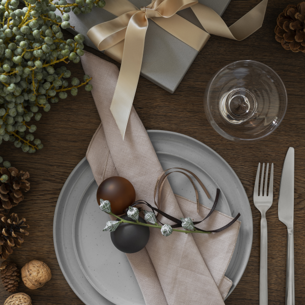 Elegante Tischdekoration für die Feiertage mit festlichen Dekorationen, einschließlich Ornamenten und einem verpackten Geschenk.