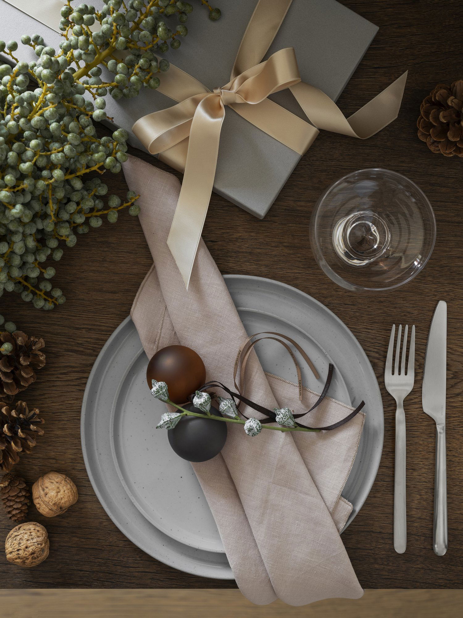 Elegante Tischdekoration für die Feiertage mit festlichen Dekorationen, einschließlich Ornamenten und einem verpackten Geschenk.
