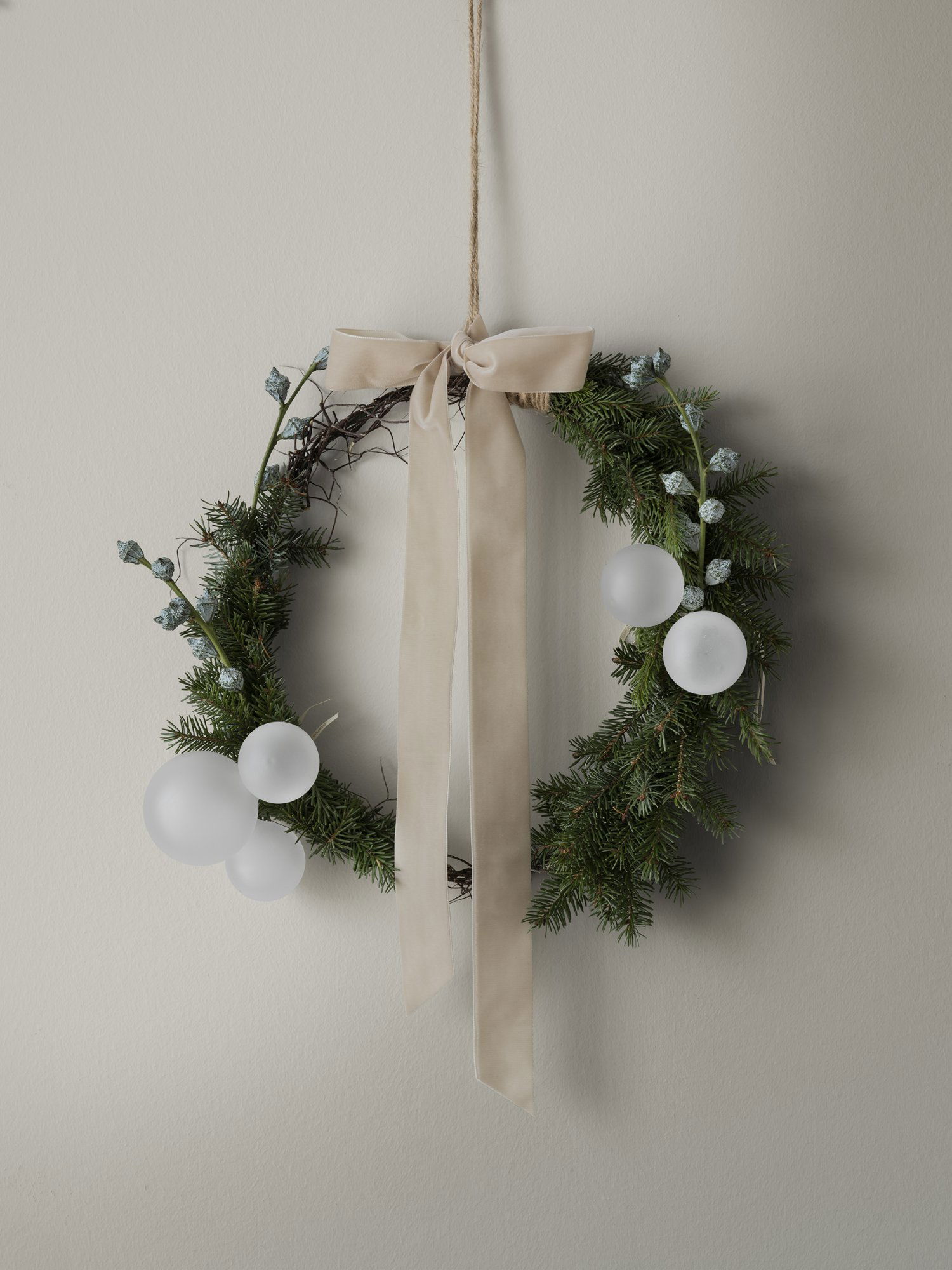 Eleganter Feiertagskranz mit weißen Ornamenten und einem sanften Band, perfekt für festliche Dekoration.