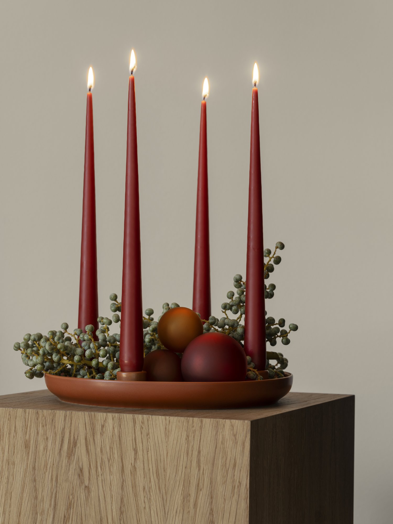 Elegantes Feiertagszentrumstück mit roten Kerzen und dekorativen Kugeln auf einem Holztisch.