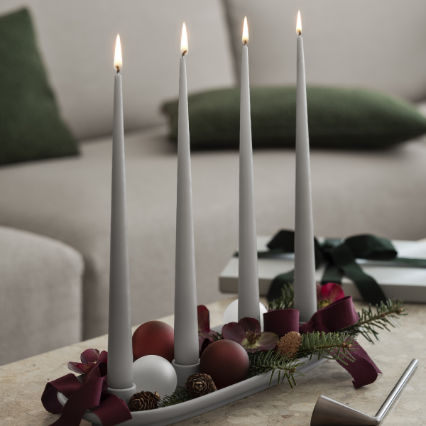 Elegantes Feiertagsmittelstück mit vier brennenden Kerzen, dekoriert mit Ornamenten und Grünpflanzen.