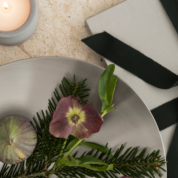 Elegant table setting with greenery, a flower, a fig, and a candle on a textured surface.