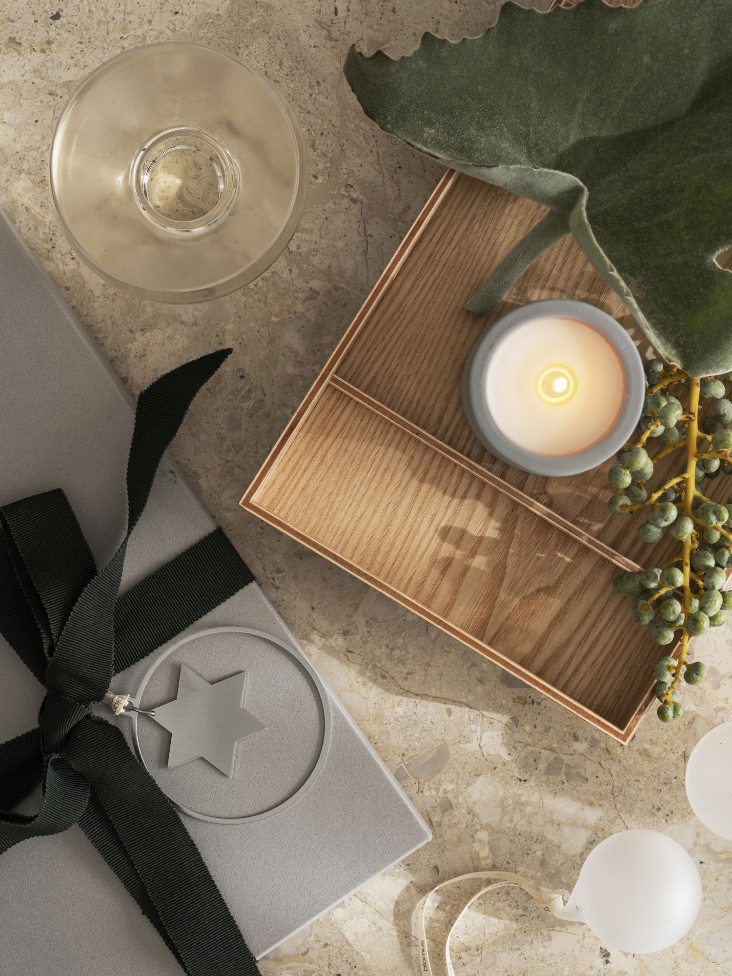 Trendige Geschenkschachtel mit eleganter Kerze, Grünpflanzen und dekorativen Elementen auf einer Marmoroberfläche.