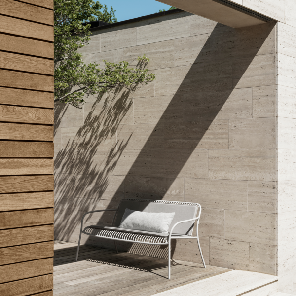 Moderne Außen-Sitzarea mit Natursteinmauer und sanften Schatten von umliegendem Grün.