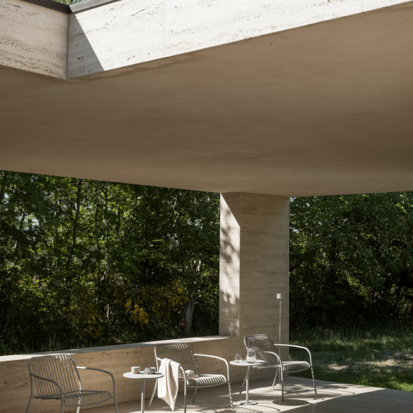 Moderner Patio mit minimalistischen Stühlen, natürlichem Licht und üppigem Grün im Hintergrund.
