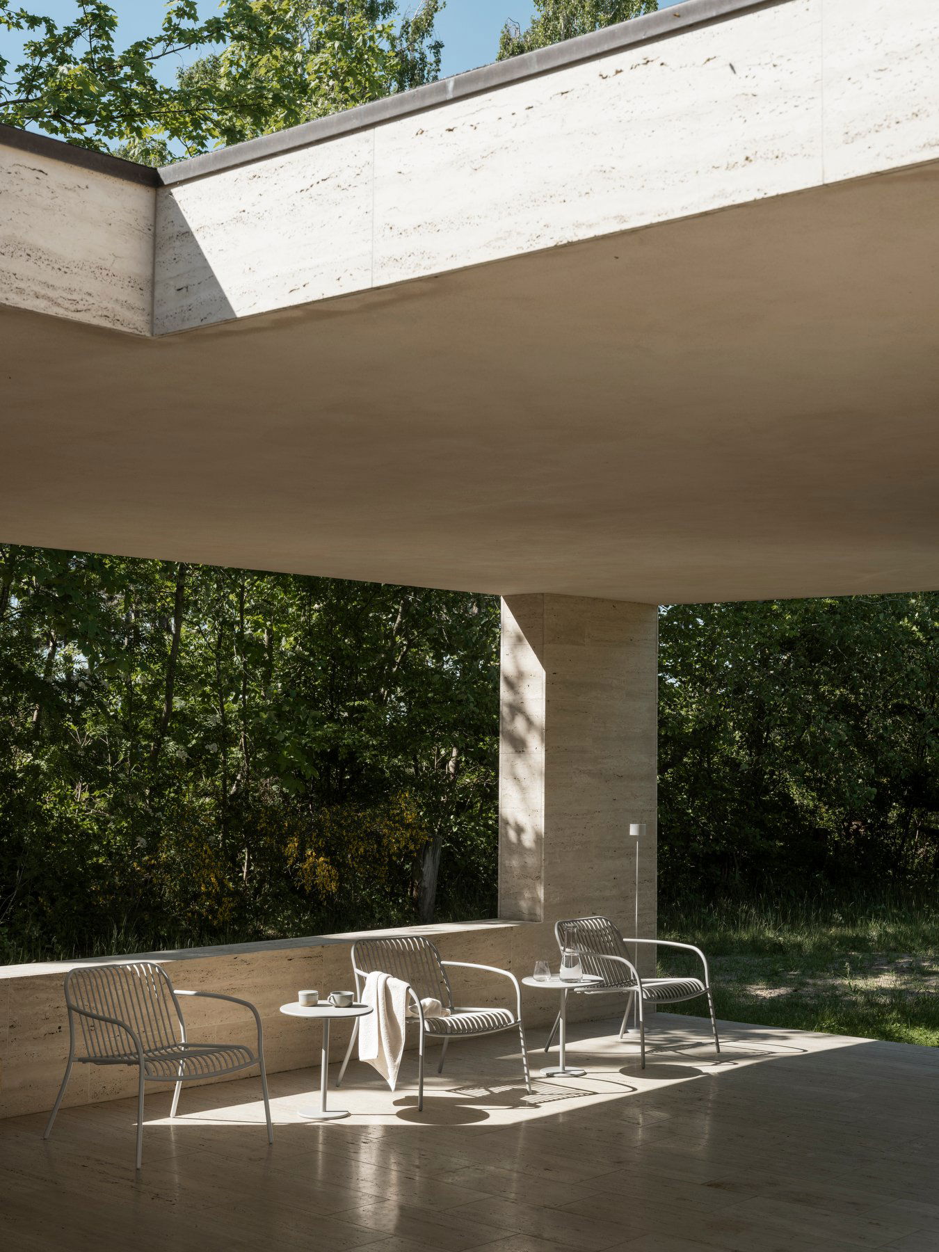 Moderner Patio mit minimalistischen Stühlen, natürlichem Licht und üppigem Grün im Hintergrund.