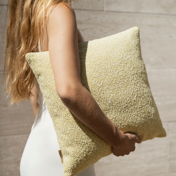 "Person holding a textured yellow pillow against a neutral background."