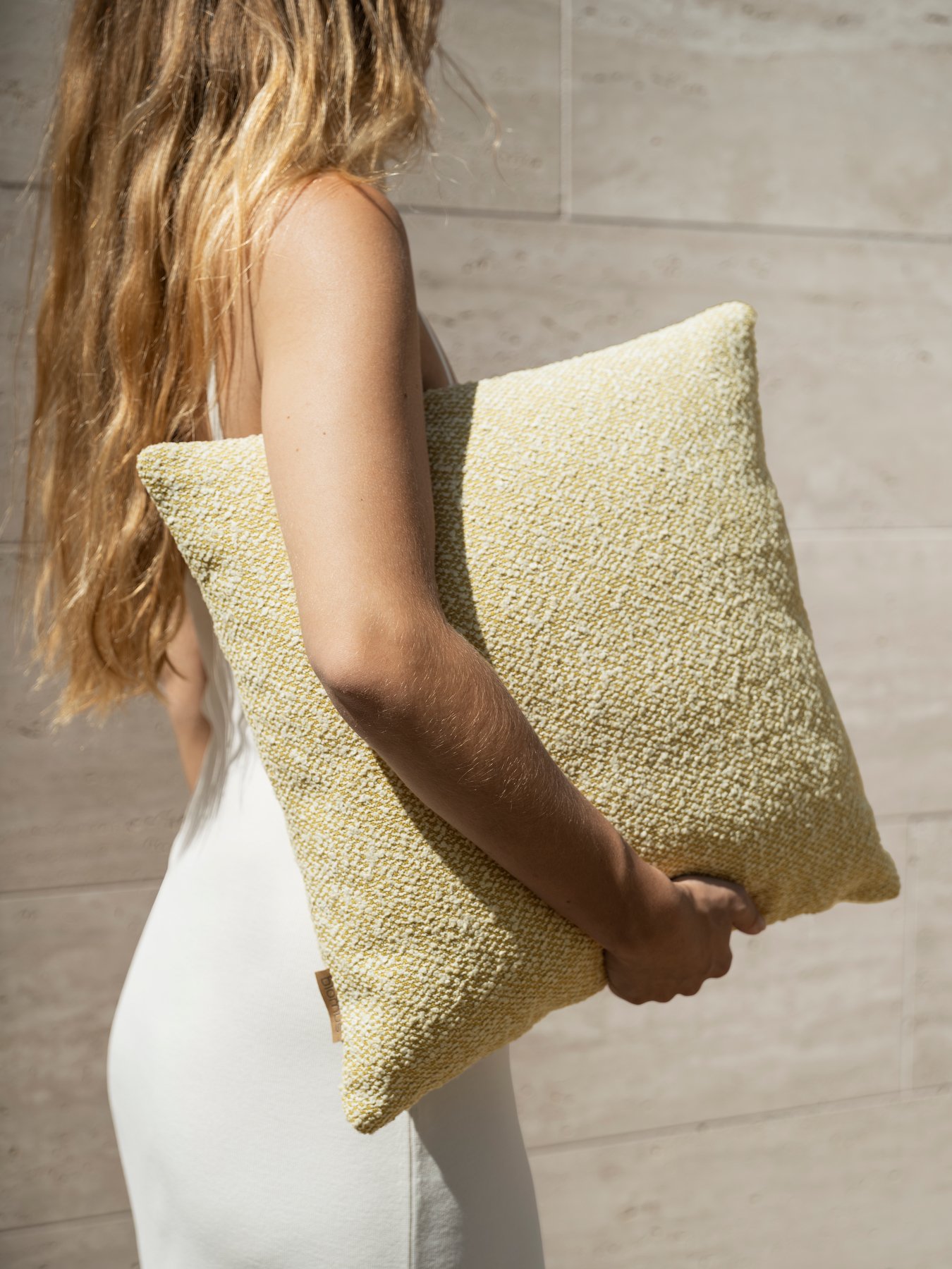 "Person holding a textured yellow pillow against a neutral background."
