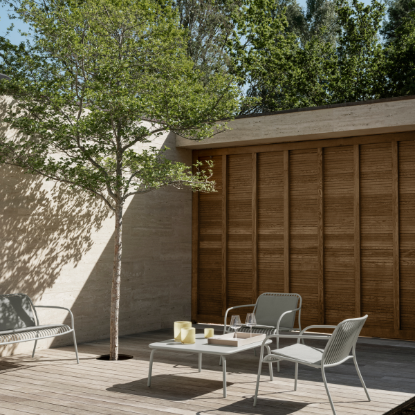 Moderner Außenpatio mit minimalistischen Möbeln und einem Baum, umgeben von üppigem Grün.