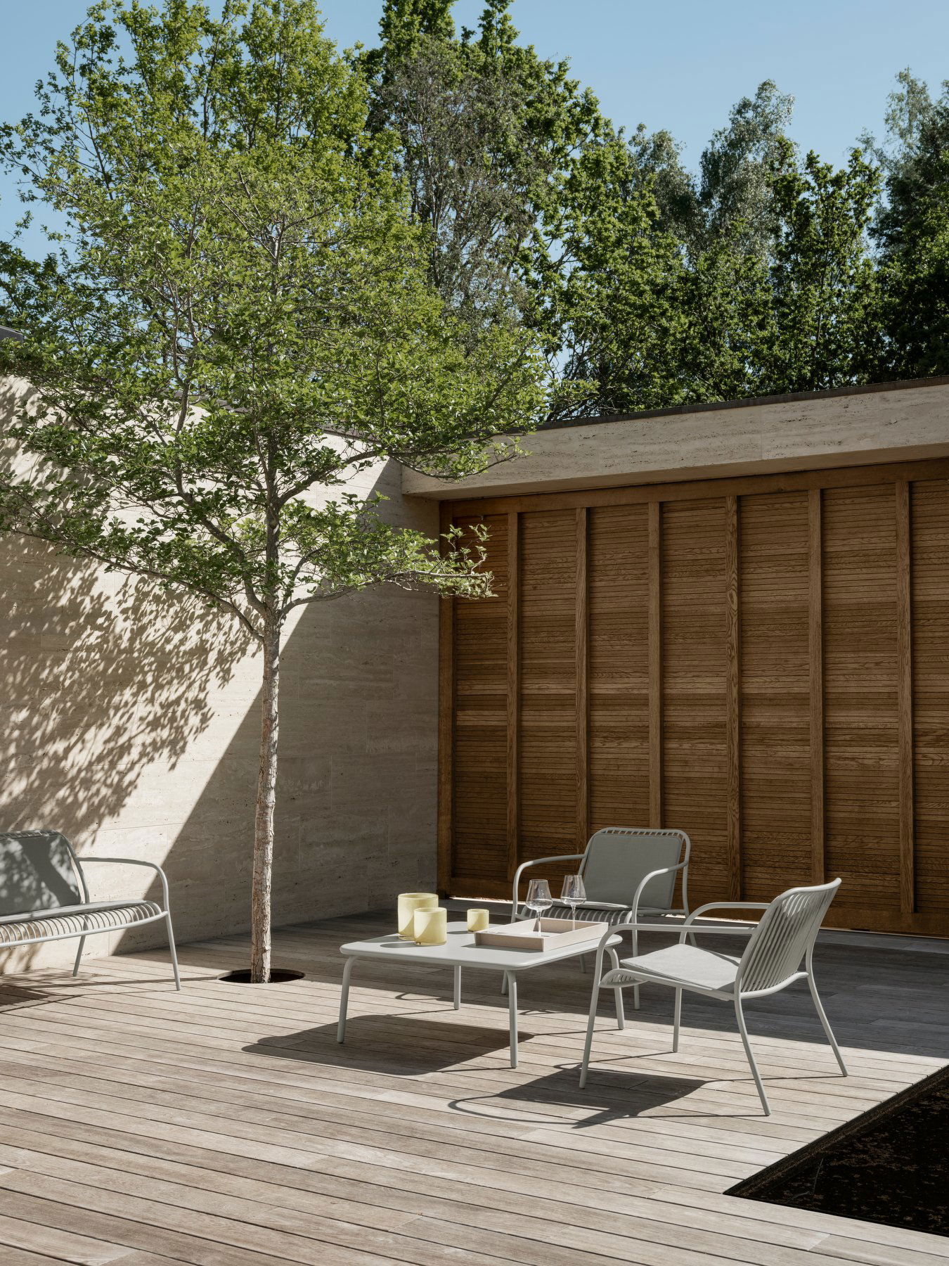Moderner Außenpatio mit minimalistischen Möbeln und einem Baum, umgeben von üppigem Grün.