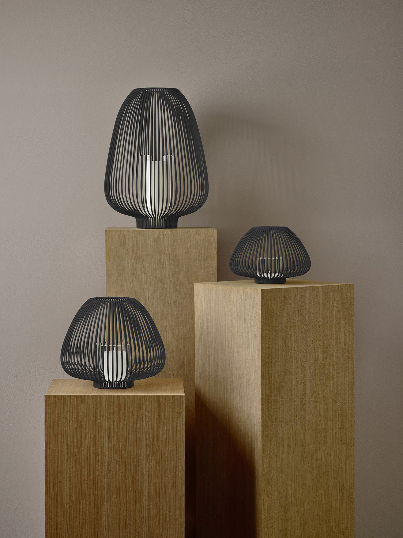Stilvolle moderne Lampen in Schwarz auf Holzpodesten vor einem neutralen Wandhintergrund.