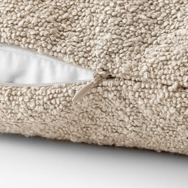 Weicher beige Kissenbezug mit einem Reißverschlussdetail auf einem strukturierten Stoff.