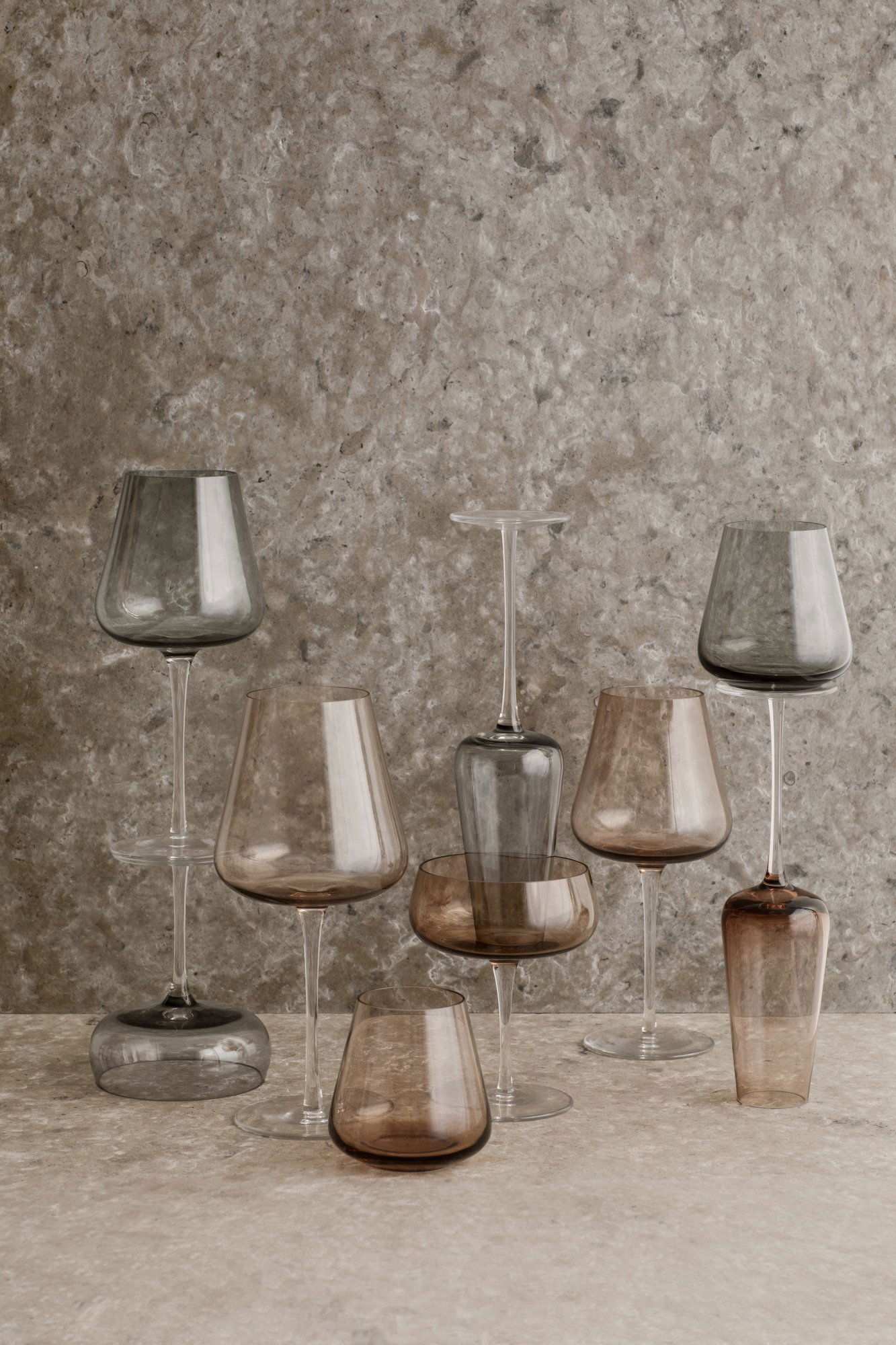 Elegante Auswahl an modernem Glasgeschirr in verschiedenen Formen und Farben auf einer strukturierten Oberfläche.