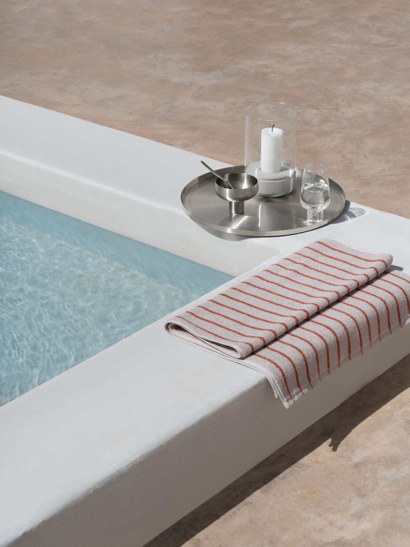 Moderne Poolumgebung mit einem gestreiften Handtuch, einem Wasserglas und einer Kerze auf einem silbernen Tablett.