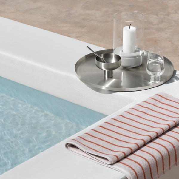 Elegante Poolside-Anordnung mit Handtuch, Kerze und Glas auf einem stilvollen Tablett am Wasser.