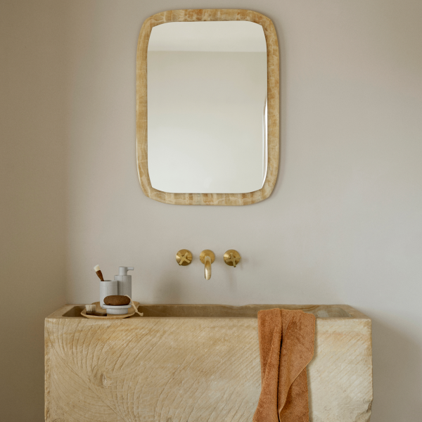 Elegantes Steingeschirrwaschbecken mit goldenen Armaturen und einem strukturierten Spiegel darüber.