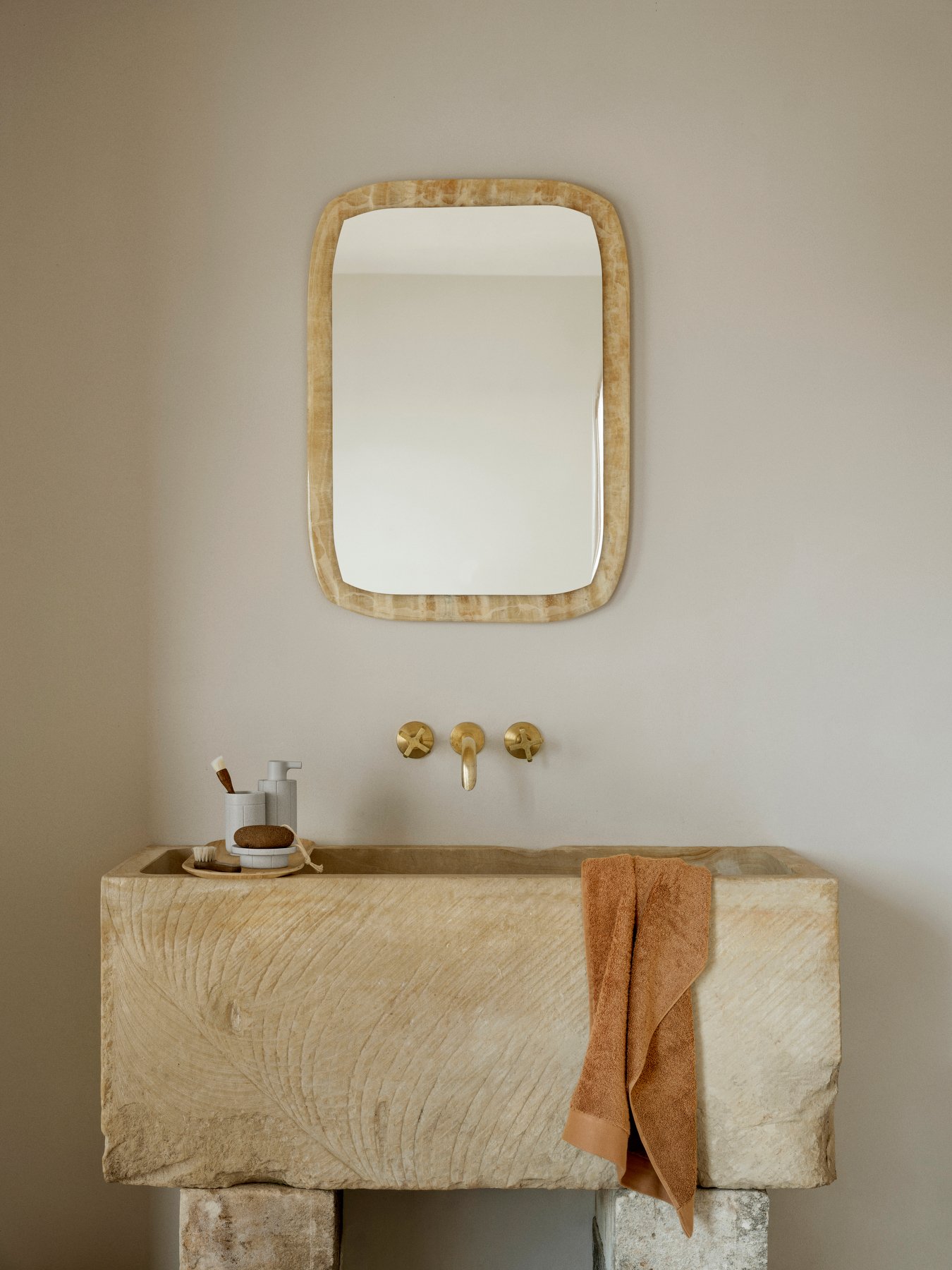 Elegantes Steingeschirrwaschbecken mit goldenen Armaturen und einem strukturierten Spiegel darüber.