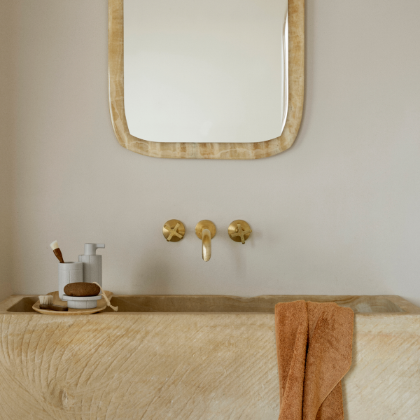 Modernes Badezimmer mit einem Steinswaschbecken, goldenen Wasserhähnen und einem strukturierten Spiegel.
