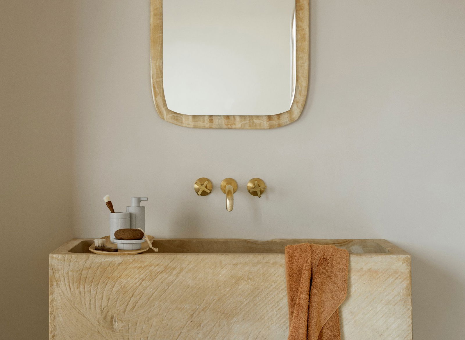 Modernes Badezimmer mit einem Steinswaschbecken, goldenen Wasserhähnen und einem strukturierten Spiegel.
