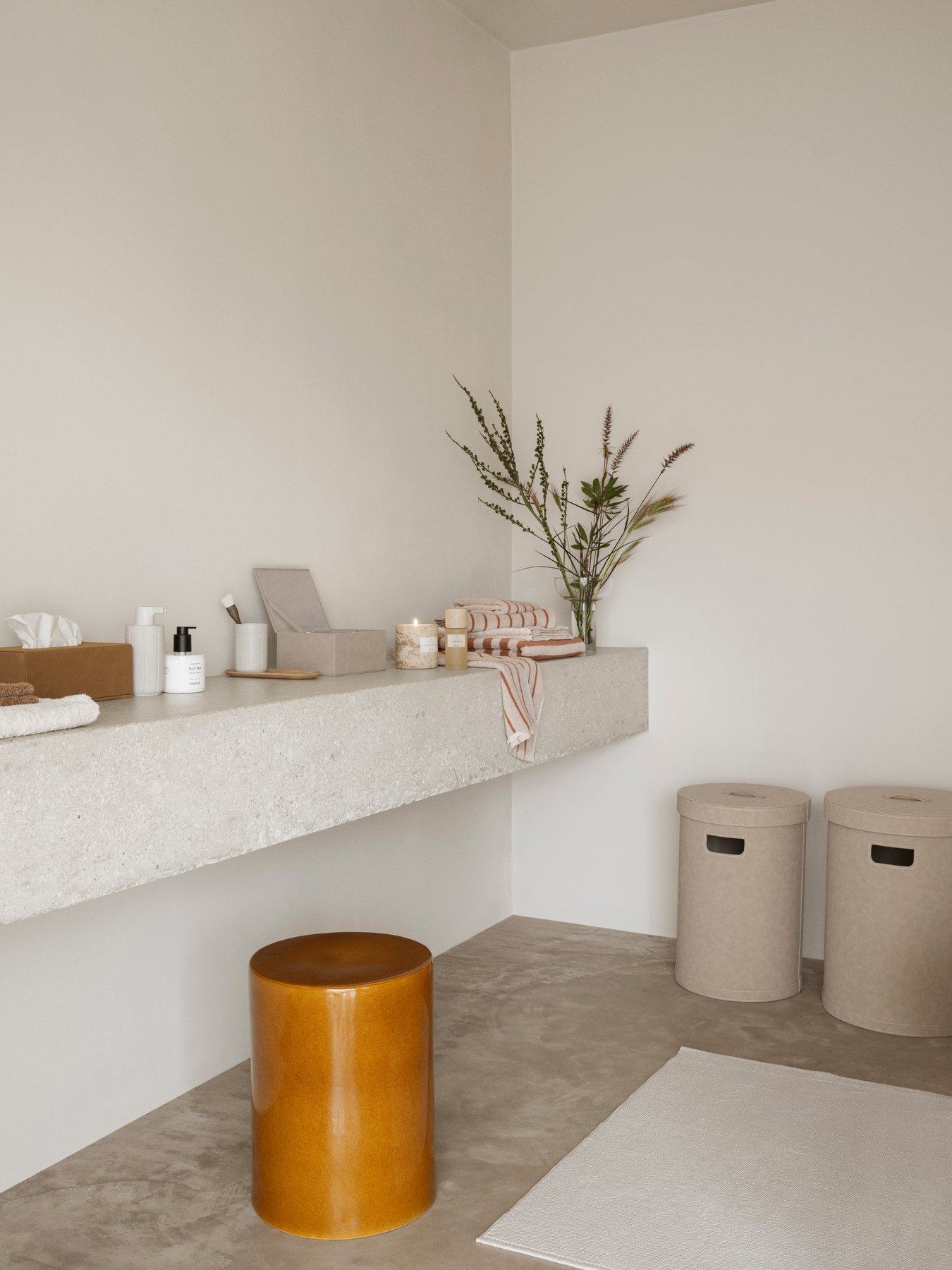 Stylish minimalist bathroom decor with a concrete shelf, candles, and decorative plants.