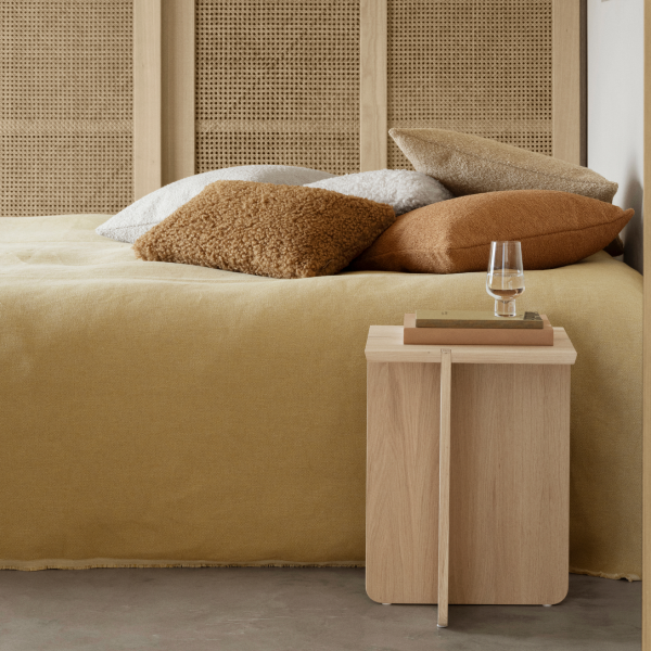 Gemütliches Schlafzimmer mit einem minimalistischen Holznachttisch und dekorativen Kissen auf einem weichen Bett.