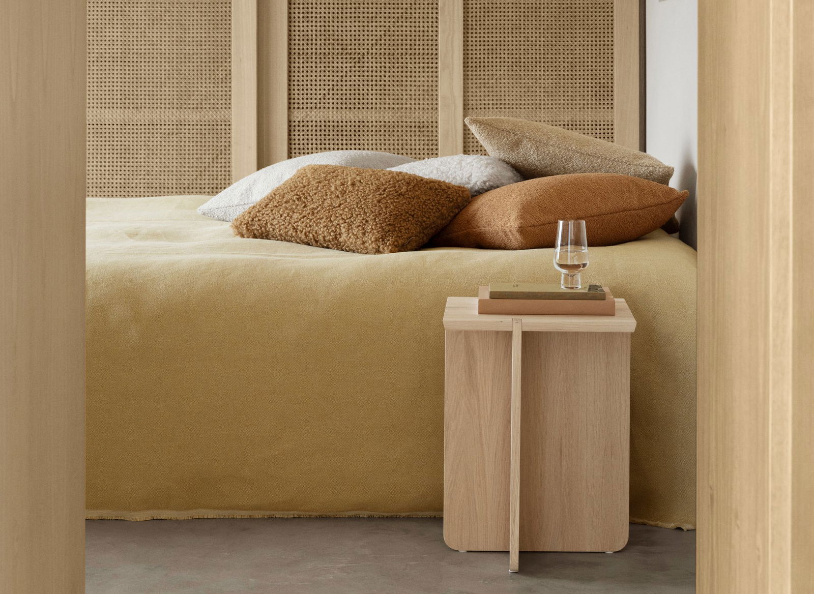 Gemütliches Schlafzimmer mit einem minimalistischen Holznachttisch und dekorativen Kissen auf einem weichen Bett.