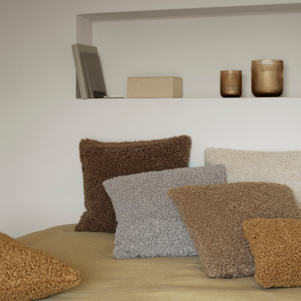 Gemütliche Wohnzimmer-Szene mit Plüschkissen in neutralen Farbtönen auf einem sanft strukturierten Bett.