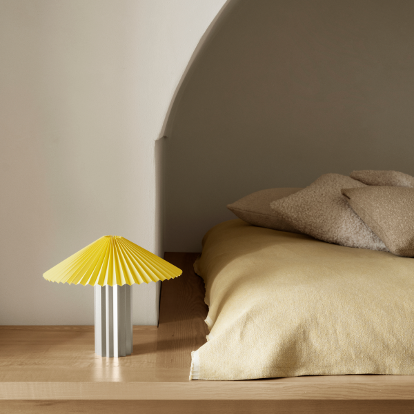Stilvolle gelbe Lampe auf einem Holz-Nachttisch neben einem gemütlichen Bett mit neutraler Bettwäsche.