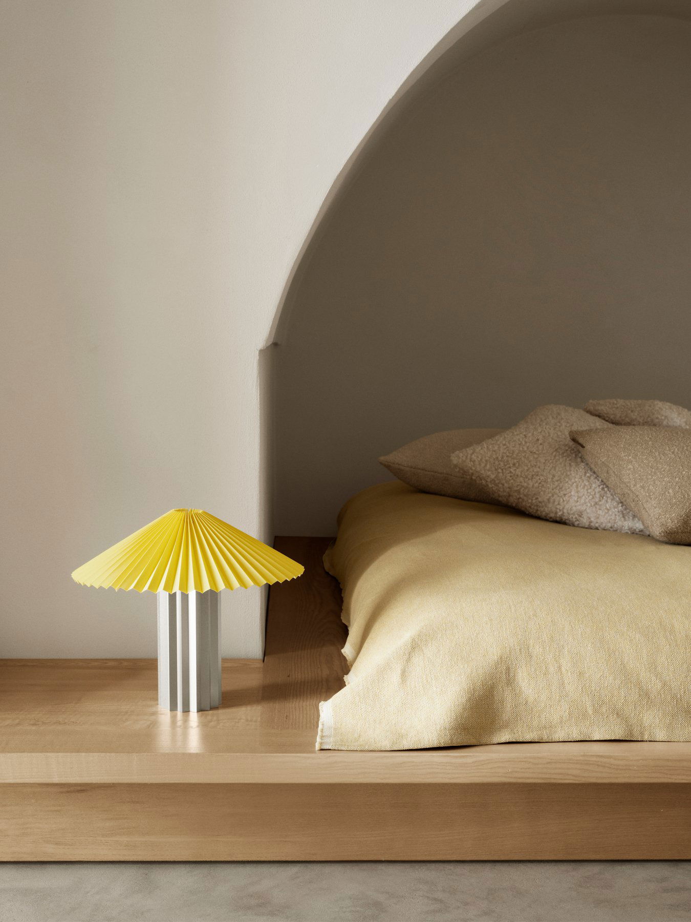 Stilvolle gelbe Lampe auf einem Holz-Nachttisch neben einem gemütlichen Bett mit neutraler Bettwäsche.