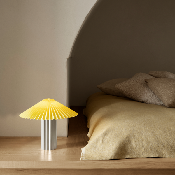 Moderne gelbe Lampe auf dem Nachttisch mit gemütlicher Bettwäsche in einem sanft beleuchteten Schlafzimmer.