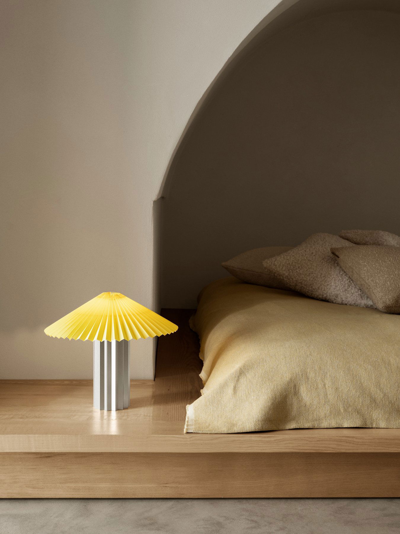 Moderne gelbe Lampe auf dem Nachttisch mit gemütlicher Bettwäsche in einem sanft beleuchteten Schlafzimmer.