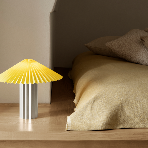 Helles gelbes Papierlicht neben einem gemütlichen Bett mit weichen Kissen in einem ruhigen Schlafzimmer.