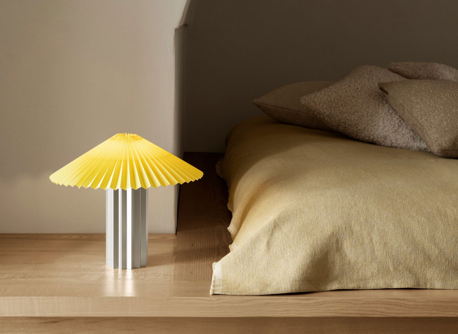 Helles gelbes Papierlicht neben einem gemütlichen Bett mit weichen Kissen in einem ruhigen Schlafzimmer.