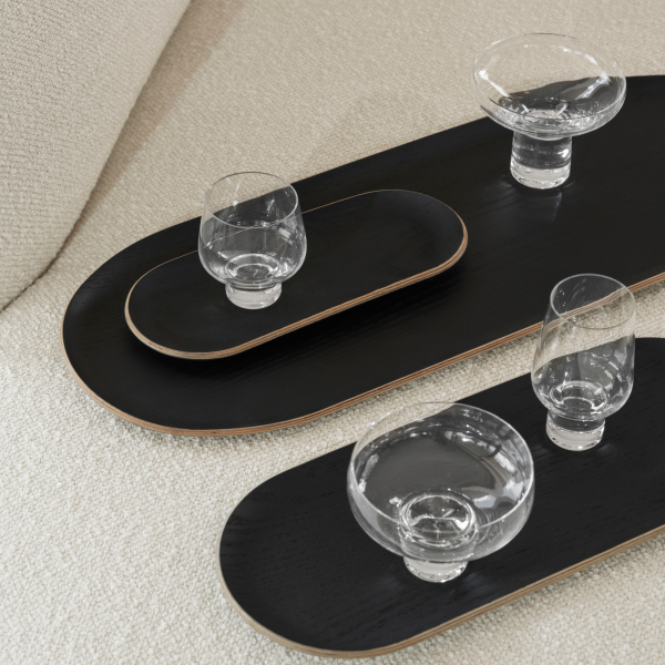Elegant black serving trays with crystal glasses on a plush beige sofa.
