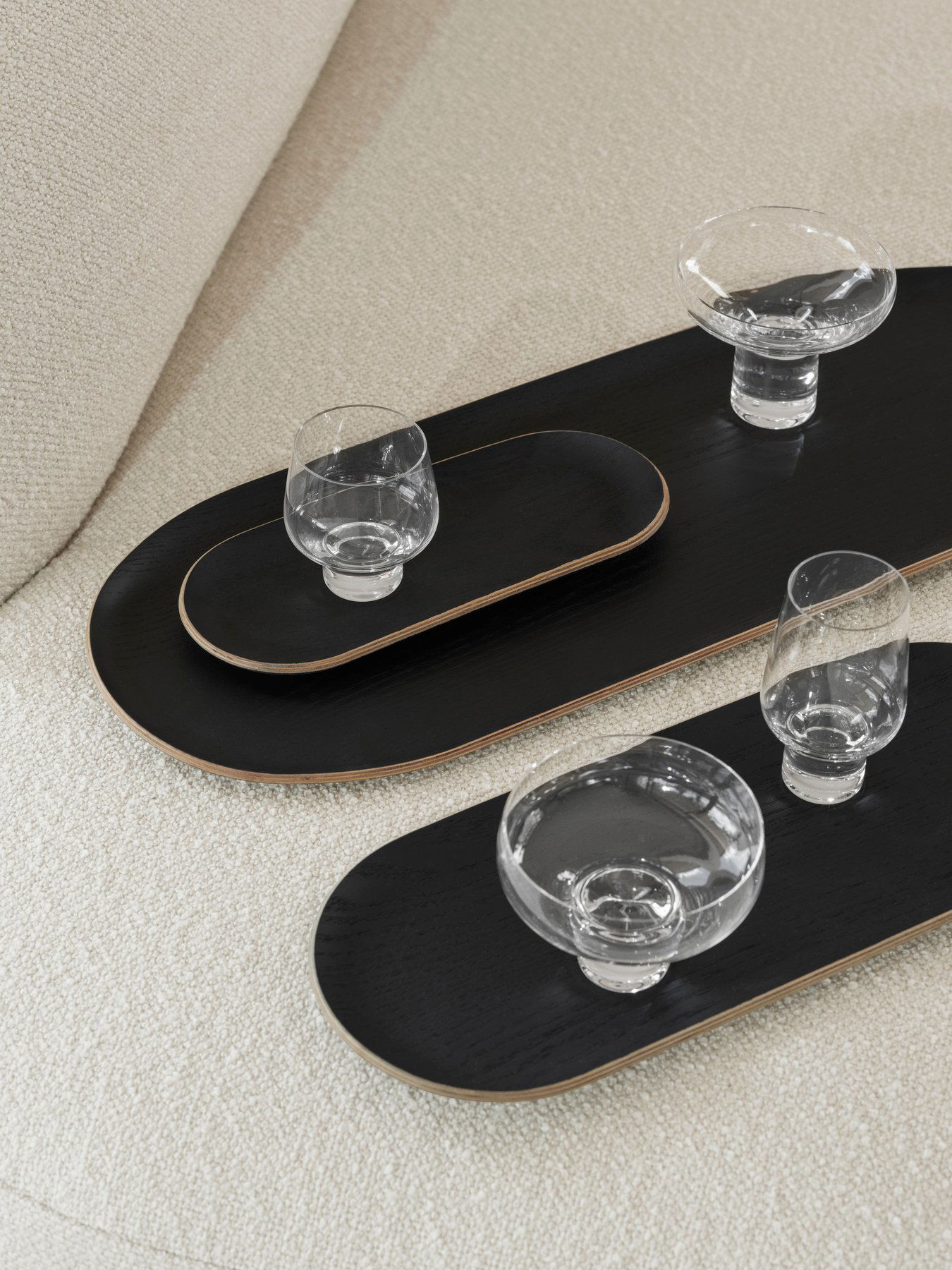 Elegant black serving trays with crystal glasses on a plush beige sofa.