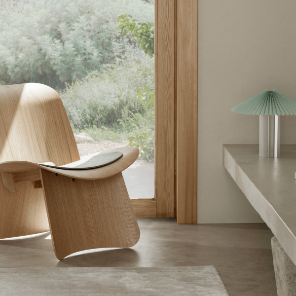 Stylischer Holzstuhl und moderne Lampe in einem ruhigen, gut beleuchteten Innenraum.