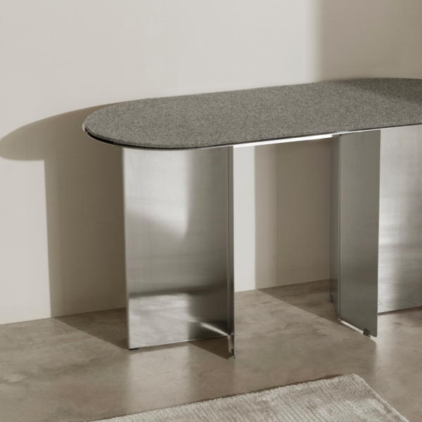 Eleganter moderner Tisch mit einer grauen Steintischplatte und Edelstahlbeinen in einem minimalistischen Ambiente.