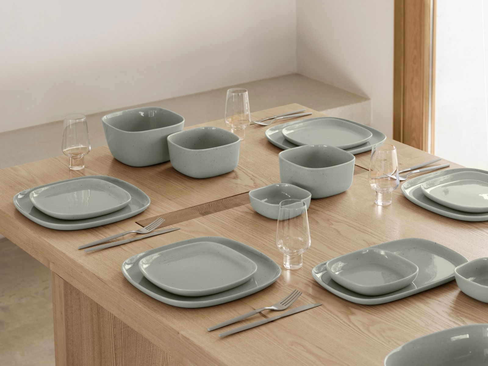 Modernes Esstischset mit hellblauen Keramiktellern und stilvollen Gläsern.