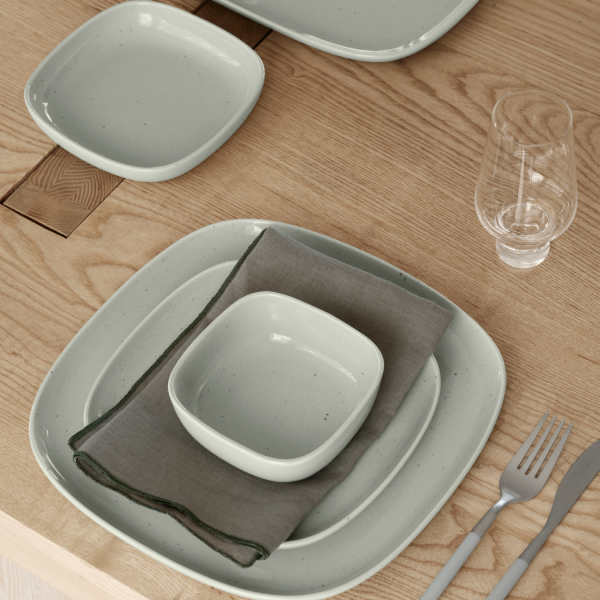 Elegantes hellgrünes Keramikteller-Set, das auf einem Holztisch mit einer Leinenserviette angeordnet ist.