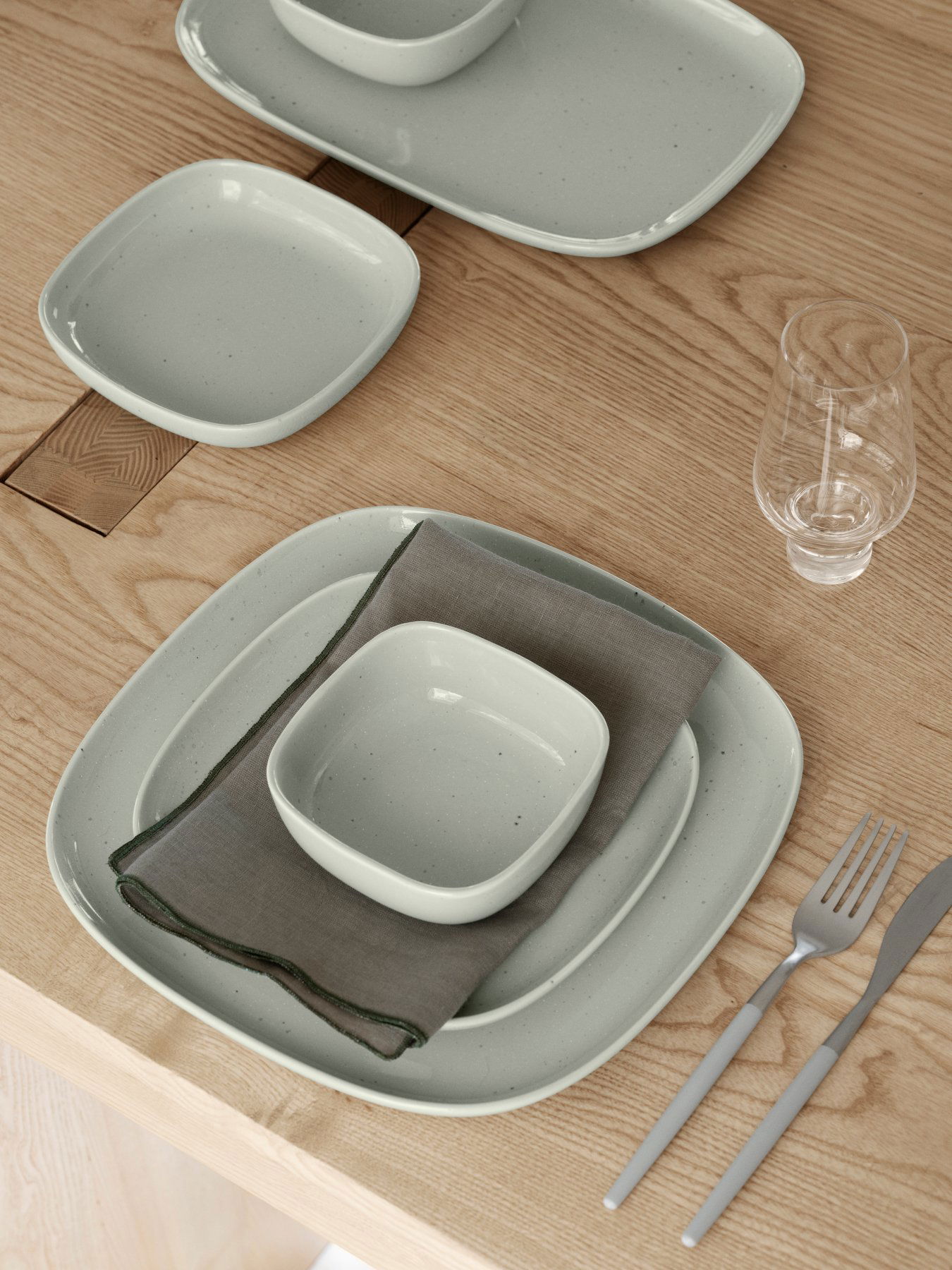 Elegantes hellgrünes Keramikteller-Set, das auf einem Holztisch mit einer Leinenserviette angeordnet ist.