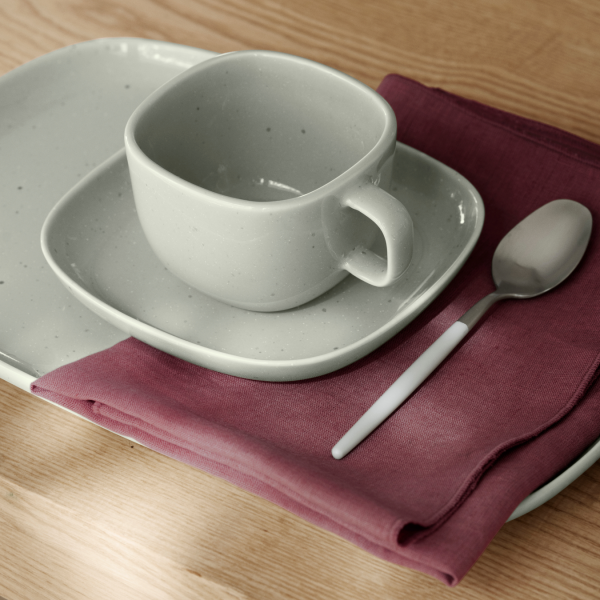 Elegant gray ceramic cup and saucer on a wooden table with a napkin and spoon.