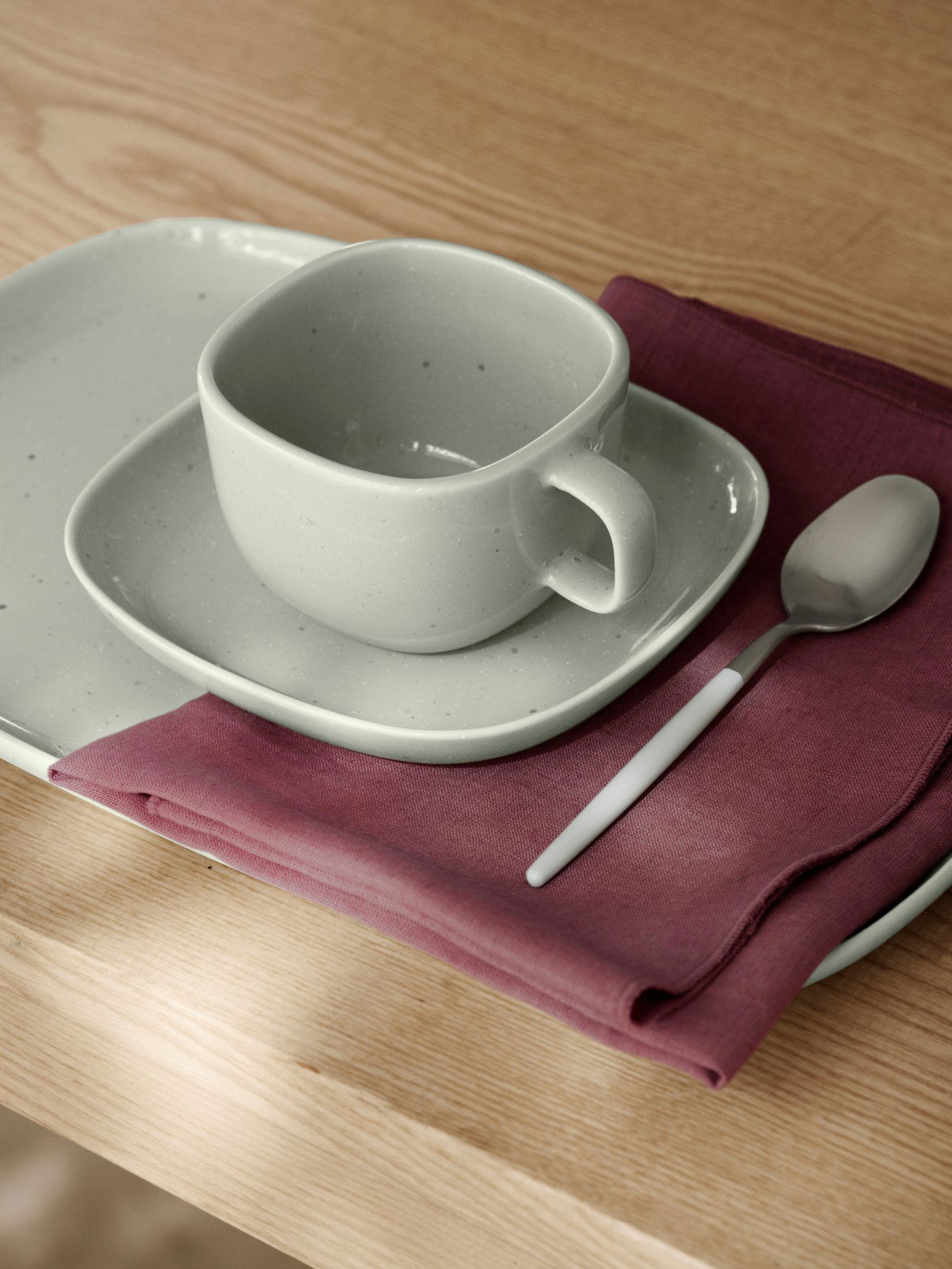 Elegant gray ceramic cup and saucer on a wooden table with a napkin and spoon.