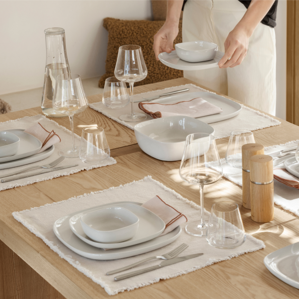 Elegante Tischdekoration mit weißem Geschirr, Gläsern und einem minimalistischen Holztisch.