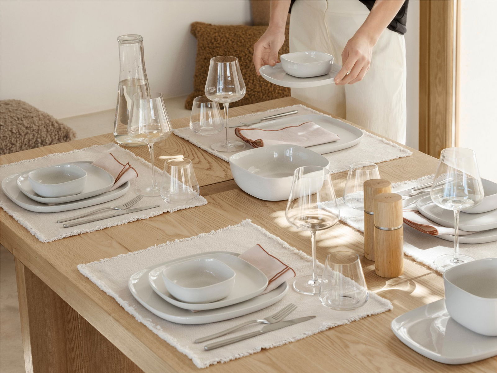Elegante Tischdekoration mit weißem Geschirr, Gläsern und einem minimalistischen Holztisch.