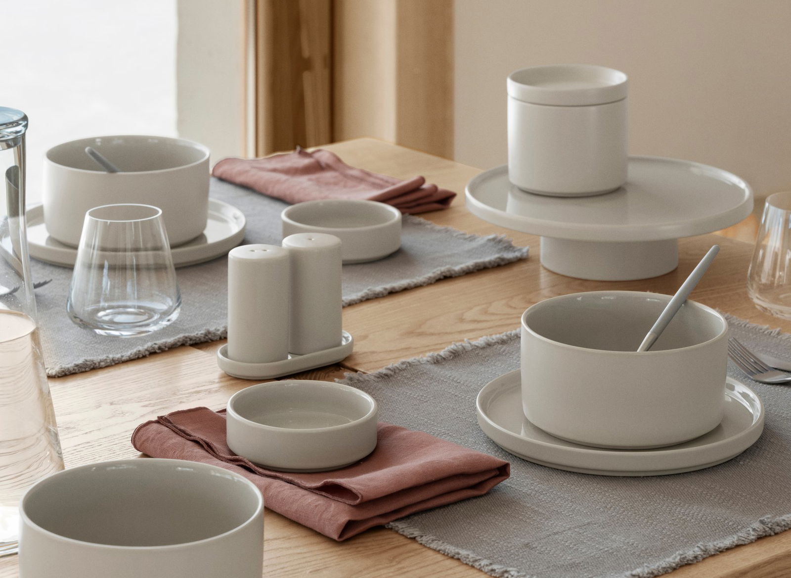 Elegante Tischdeko mit minimalistischem grauen Geschirr und weichen Leinenservietten.