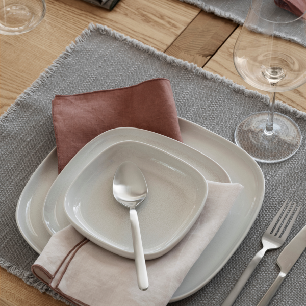 Elegante Tischeinrichtung mit weißen Tellern, pastellfarbenen Servietten und Gläsern auf einem grauen Tischset.