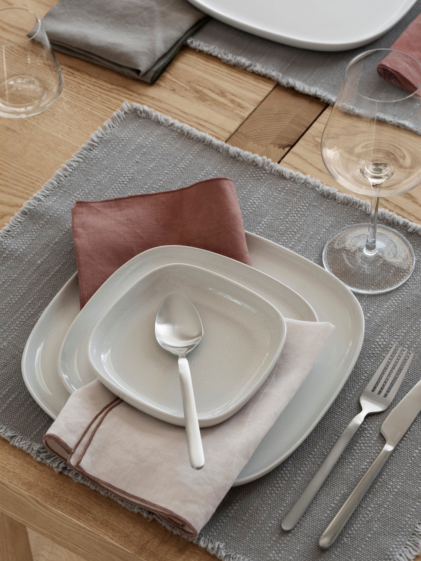Elegante Tischeinrichtung mit weißen Tellern, pastellfarbenen Servietten und Gläsern auf einem grauen Tischset.