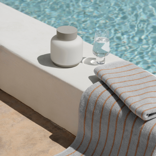 Stilvolles Poolsetup mit einem Glas Wasser, einer Keramikkaraffe und einem gestreiften Handtuch.