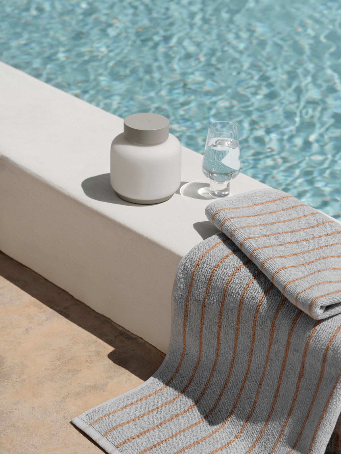 Stilvolles Poolsetup mit einem Glas Wasser, einer Keramikkaraffe und einem gestreiften Handtuch.