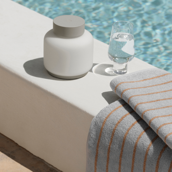 Elegante Poollandschaft mit einem weißen Behälter, einem Glas Wasser und einem gestreiften Handtuch.